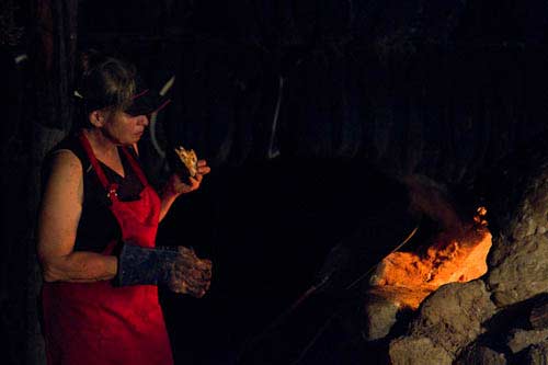 A pizza maker tastes her product as she stares into the oven